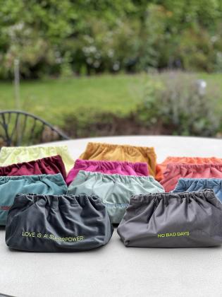 Gesamtfoto: Mehrere Samt-Taschen in kräftigen Farben mit aufgestickten Sprüchen, nebeneinander arrangiert. 	•	Einzelfotos: Jeweils eine Samt-Tasche in leuchtender Farbe mit dem Spruch [Slogan] vorne aufgestickt, wasserfest gefüttert.